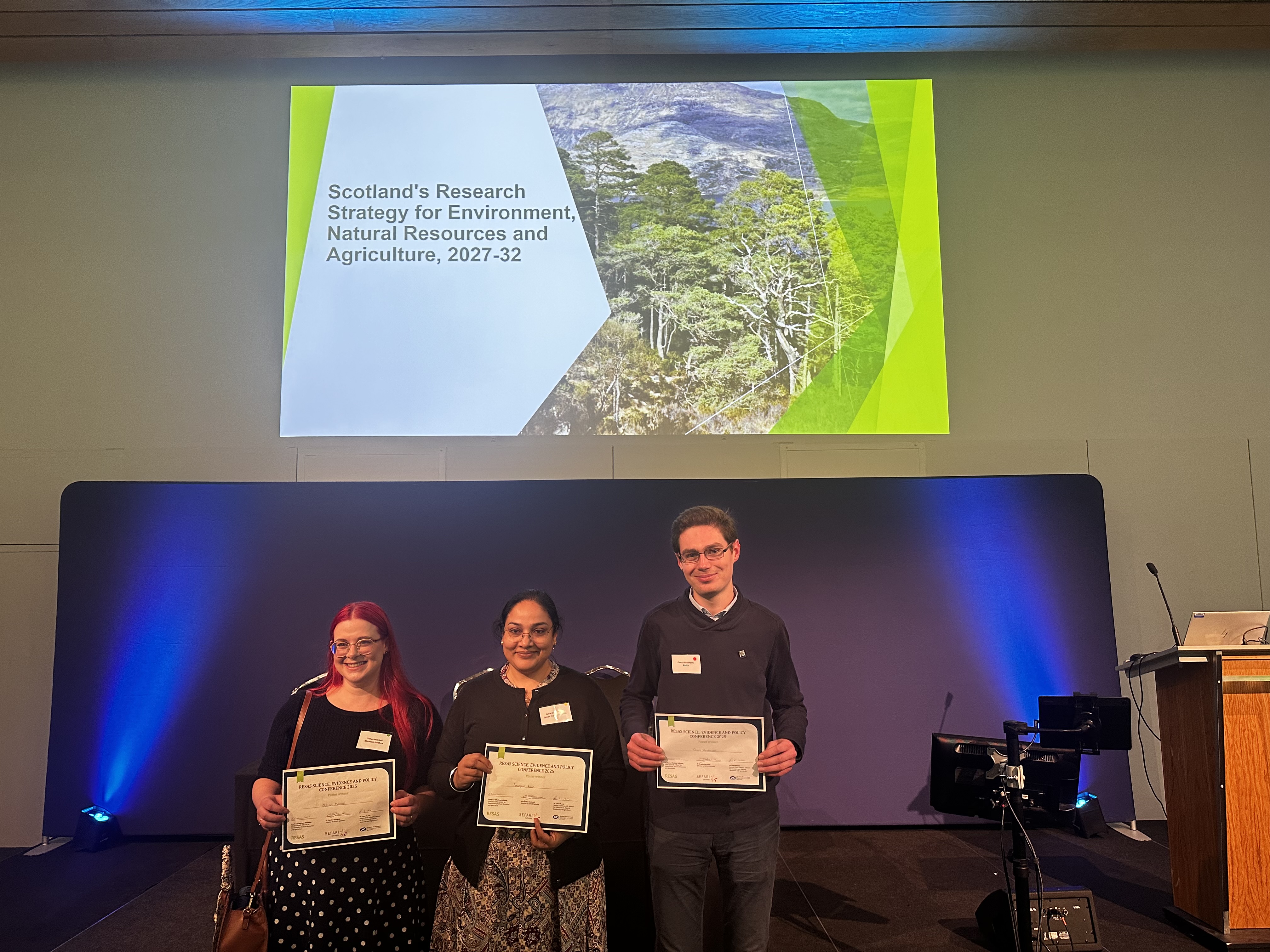 Three people stand in front of a podium with certificates.